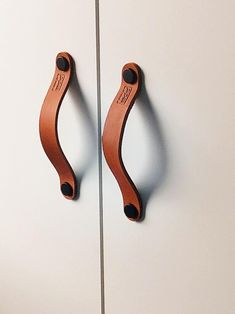 two wooden handles hang on the side of a white cabinet with black knobs and an orange leather handle