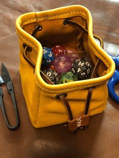 a pair of scissors and some dice in a yellow bag on a table next to a pair of blue handled scissor