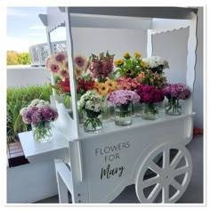 flowers are arranged in mason jars on a white cart with the word flowers for mary painted on it