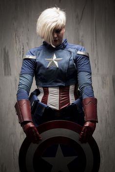 a woman dressed as captain america standing in front of a concrete wall with her hands on her hips