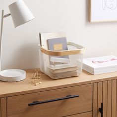 a desk with a lamp, books and other items on it next to a dresser