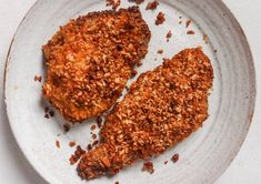 two pieces of fried chicken on a plate with crumbled crusts and seasoning