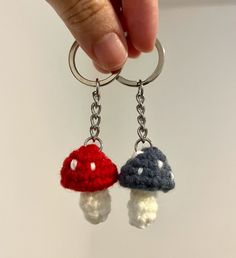 two crocheted mushroom key chains being held by a person's hand on a white surface