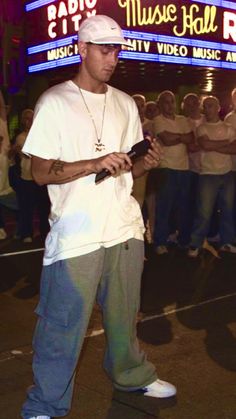 a man standing in front of a crowd holding a cell phone and wearing a white hat