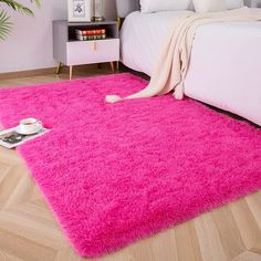 a bright pink rug is on the floor next to a bed with pillows and blankets