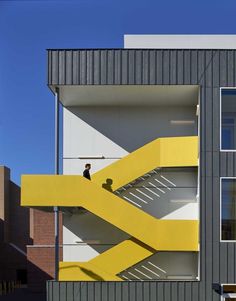 a yellow stair case on the side of a gray and white building with two people walking up it