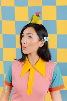 a woman with a bird on her head standing in front of a checkered wall