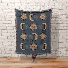 a woman standing in front of a brick wall holding up a blanket with sun and moon designs on it