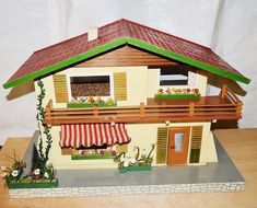 a doll house with an awning and flower boxes on the outside, in front of a white wall