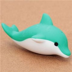 a green and white dolphin toy sitting on top of a brown surface with its mouth open