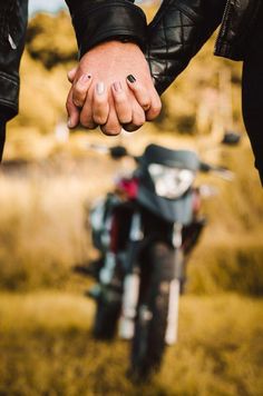 two people holding hands while standing next to a motorcycle