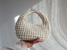 a hand holding a crocheted white purse