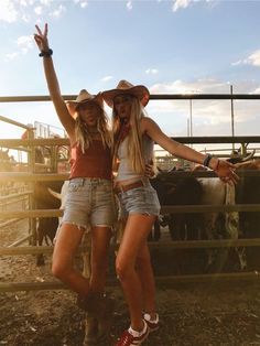 two women standing next to each other in front of a fence with cows behind them