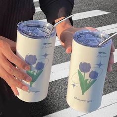 two people are holding their tumblers on the street and one is holding a straw