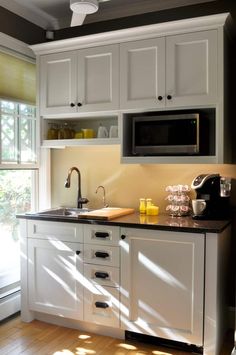 a kitchen with white cabinets and black counter tops, along with a window in the background