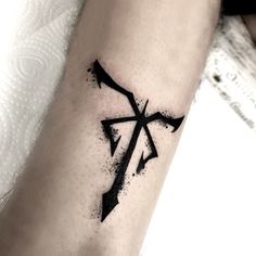 a cross tattoo on the arm with black paint splattered over it and an arrow