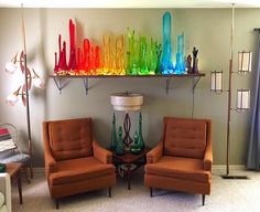 two orange chairs sitting next to each other in front of a rainbow wall decoration on the wall