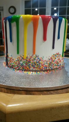 a multicolored cake with sprinkles and icing on a table