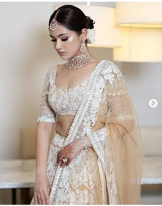 a woman in a white and gold bridal outfit with jewelry on her head, standing next to a table