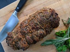 a piece of meat sitting on top of a wooden cutting board next to greens and a knife