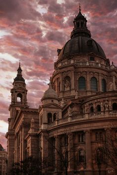 an old building with two towers under a cloudy sky at sunset or dawn in the city