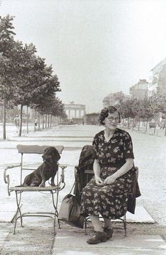 an old photo of a woman sitting on a bench with her dog next to her