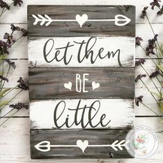 a wooden sign that says let them be little on it with hearts and arrows in the middle