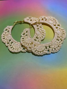 two white crocheted hoop earrings sitting on top of a rainbow colored tablecloth