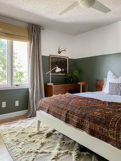 a bedroom with a bed, dresser and ceiling fan in front of a window that looks out onto the woods