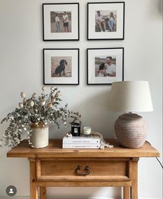 three framed pictures hang on the wall above a table with a lamp and vase filled with flowers