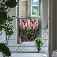 a bath tub sitting under a window next to a potted plant