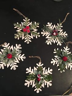 four snowflake ornaments with holly and red berries hanging from twine on black board