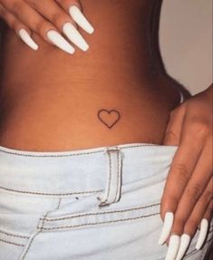 a woman with white nails and a heart tattoo on her stomach is holding onto her jeans