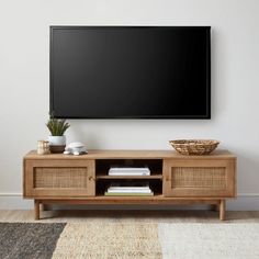 a flat screen tv mounted on the wall above a wooden entertainment center with wicker baskets