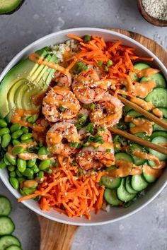 a bowl filled with shrimp, carrots and cucumber next to sliced avocado