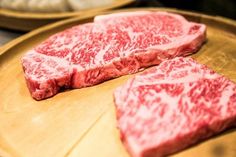 two pieces of raw meat sitting on top of a wooden plate