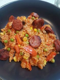 a black plate topped with rice and sausage