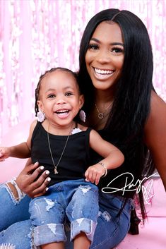 a woman holding a child in her lap and smiling at the camera with pink background