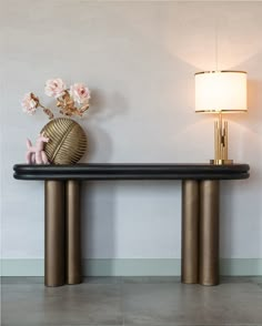 a vase with flowers sitting on top of a black table next to a gold lamp