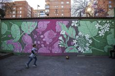 a person walking in front of a wall with flowers painted on it and buildings behind