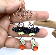 a hand holding a pair of earrings with black and white designs on the front, orange beads in the back