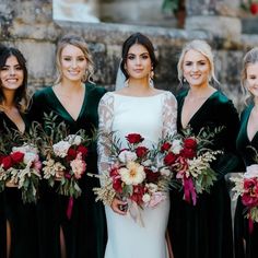 a group of women standing next to each other in front of a stone wall holding bouquets