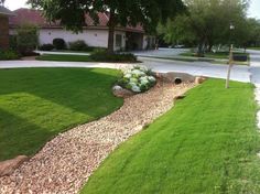 a yard with grass, rocks and flowers on the side walk in front of a house