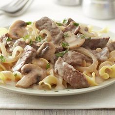 a white plate topped with pasta and meat covered in mushroom sauce on top of a table