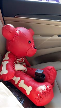 a red teddy bear sitting in the back seat of a car holding a cell phone