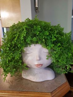 the head of a mannequin is covered with green leaves and foliage as it sits on a table