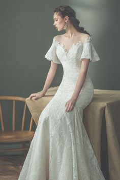 a woman in a white wedding dress sitting on a table with her hand on her hip