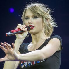 a woman holding a microphone in her right hand and wearing a black shirt with red lettering on it