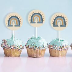 three cupcakes with frosting and rainbow toppers on them, sitting next to each other