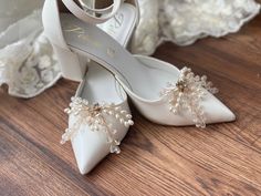 a pair of white wedding shoes with pearls on the heel and lace trimmings